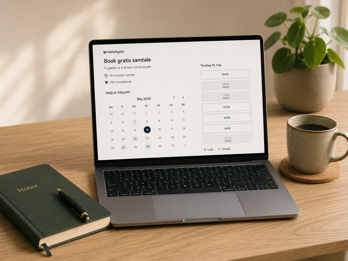 Laptop med bookingkalender og ledige tider på skrivebord med kaffekop, notesbog og plante.